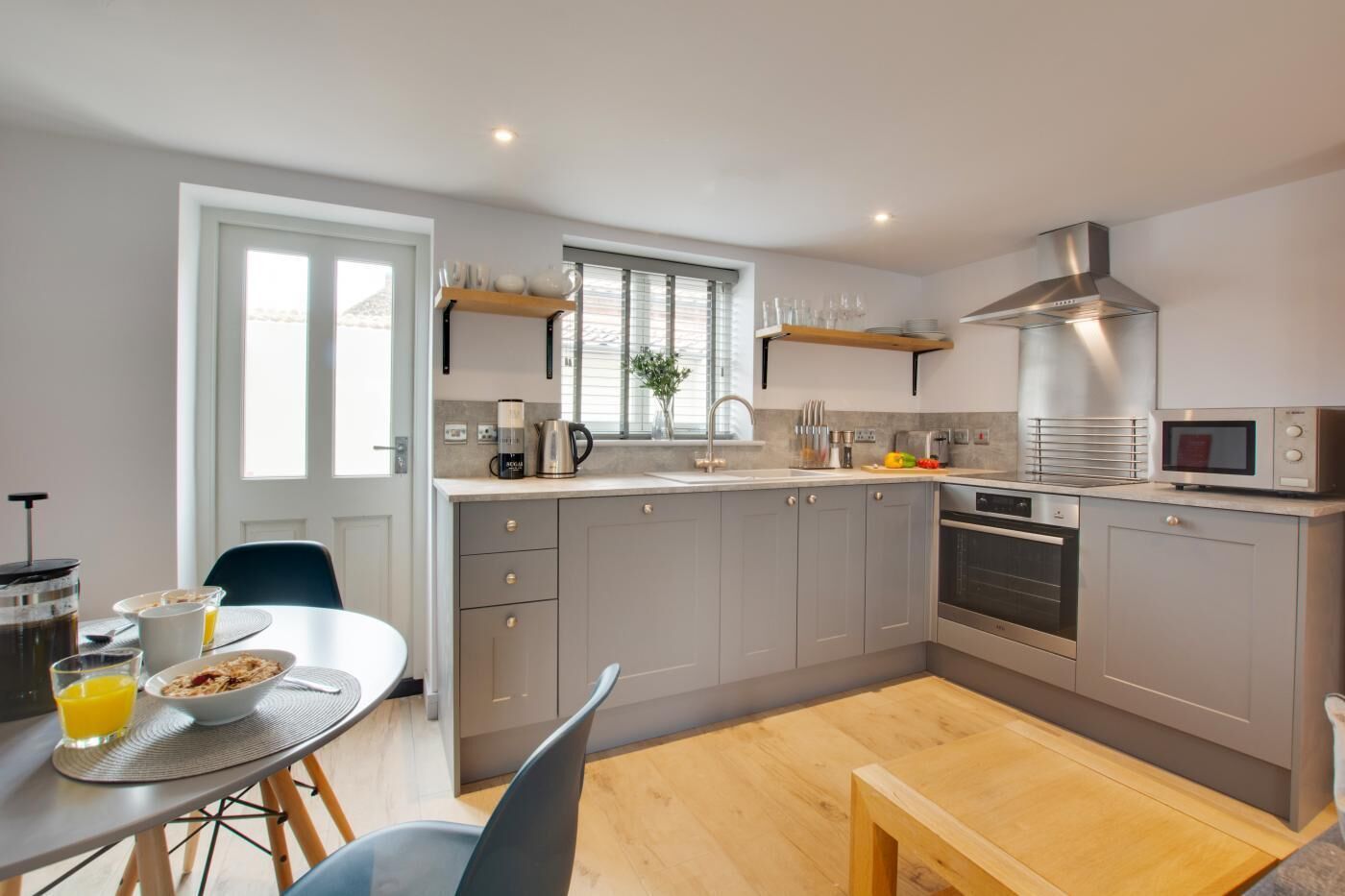 A modern kitchen with grey cabinets, a stainless steel range hood, and a microwave.