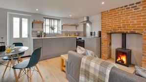 A modern kitchen with grey cabinets, a built-in oven, and a microwave. There's a dining area with a table and chairs, and a fireplace with a brick wall. - 1 Bed in Holt (oc-2185) (Holt)