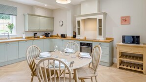 A modern kitchen with light-colored cabinets, a wooden dining table set for four, and a microwave on a wooden sideboard. - 2 Bed in Mannington (oc-g32751) (Mannington)