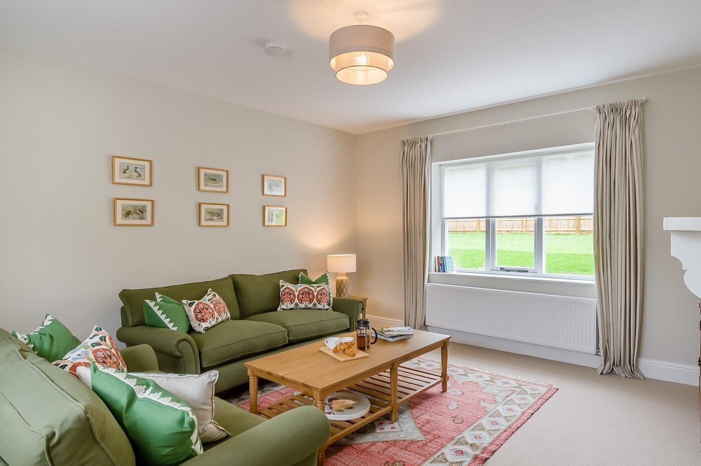 A living room with a green sofa set, a wooden coffee table, and a large window with curtains.
