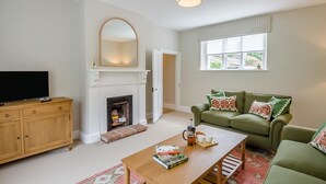 A living room with a fireplace, a television on a wooden cabinet, a green sofa with patterned cushions, and a coffee table with books and a coffee pot. - 2 Bed in Mannington (oc-g32751) (Mannington)