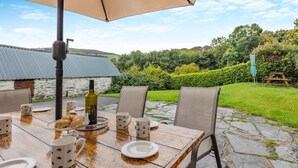 Un espace de restauration en plein air avec une table dressée pour quatre personnes, entourée de chaises, et protégée par un grand parasol.