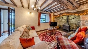 Un salon chaleureux avec un mur en pierre, une cheminée et un téléviseur posé sur une table en bois.
