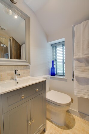 A bathroom with a white sink, a mirror, a toilet, and a window with blinds. - 1 Bed in Holt (oc-2186) (Holt)