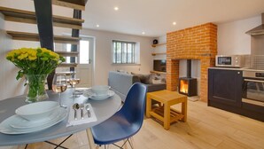 Une cuisine moderne avec une cheminée en briques, un coin repas avec une table ronde et des chaises bleues, et un salon avec un canapé et un téléviseur.