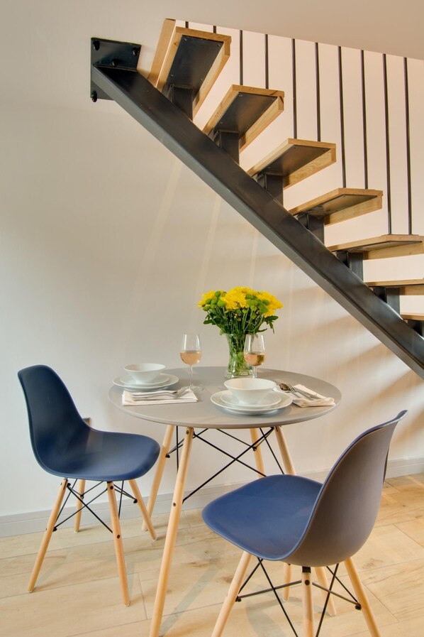 A dining area with a round table, two chairs, a vase with yellow flowers, and a glass of wine. - 1 Bed in Holt (oc-2186) (Holt)