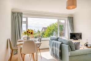 A modern living room with a dining area, large windows, a sofa, and a TV. - 3 Bed in Cowes (oc-s32705) (Cowes)