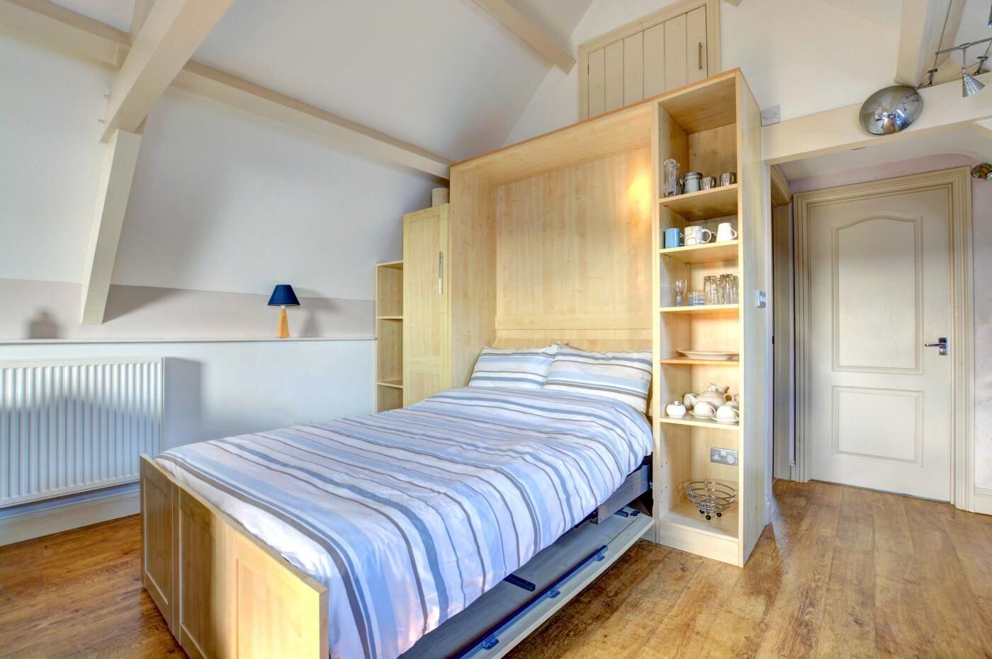 A bedroom with a bed, wooden wardrobe, and built-in shelves.