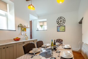 Un coin repas avec une table dressée pour quatre personnes, une horloge au mur et une fenêtre donnant sur un beau paysage.