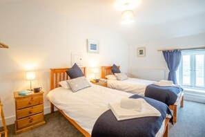 Une chambre d’hôtel avec deux lits, deux tables de chevet, une lampe, un radiateur et une fenêtre avec des rideaux.