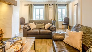 Una sala de estar acogedora con un sofá de cuero, dos sillones, una mesita de centro y una ventana con cortinas.