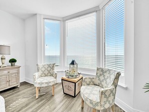 A bright room with white walls, two patterned armchairs, a wooden side table with a lamp, and a small plant. - 🏝️Beach FRONT | 2 POOLS | Hot Tub | Emerald Beach 931🏝️ (Panama City Beach)