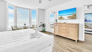 Ein geräumiges Schlafzimmer mit einem großen Bett, einem Deckenventilator, einer Holzkommode und einem Wandbild mit Strandmotiv.
