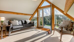 Un dormitorio estilo loft moderno con techo inclinado, un sofá, una silla y vistas al exterior.