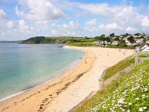 A coastal beach with a sandy shore, a clear blue sea, and a grassy area with white flowers. - 1 Bed in Falmouth (oc-theco) (Blankednick)