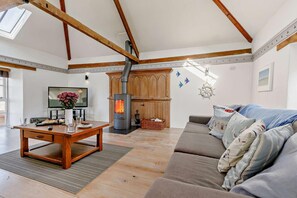 A spacious living room with a large wooden table, a sofa, and a wood-burning stove. - 2 Bed in Wadebridge (oc-p00449) (Wadebridge)