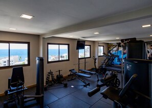 A gym with various exercise equipment, large windows with a view of the sea, and a ceiling with recessed lighting. - Cozy high floor apartment in Ondina (Salvador)