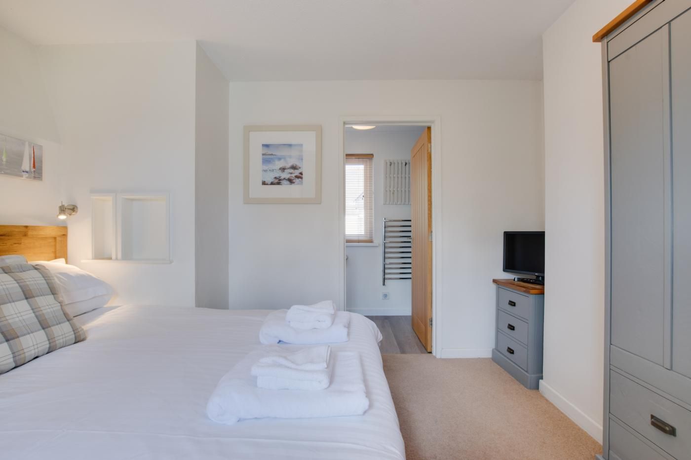 A hotel room with a bed, a TV, a wardrobe, and a framed picture on the wall.