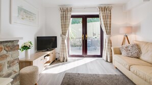 Un salon comprenant une télévision, un canapé, une lampe, une cheminée et une vue sur l’extérieur, visible à travers une porte vitrée.