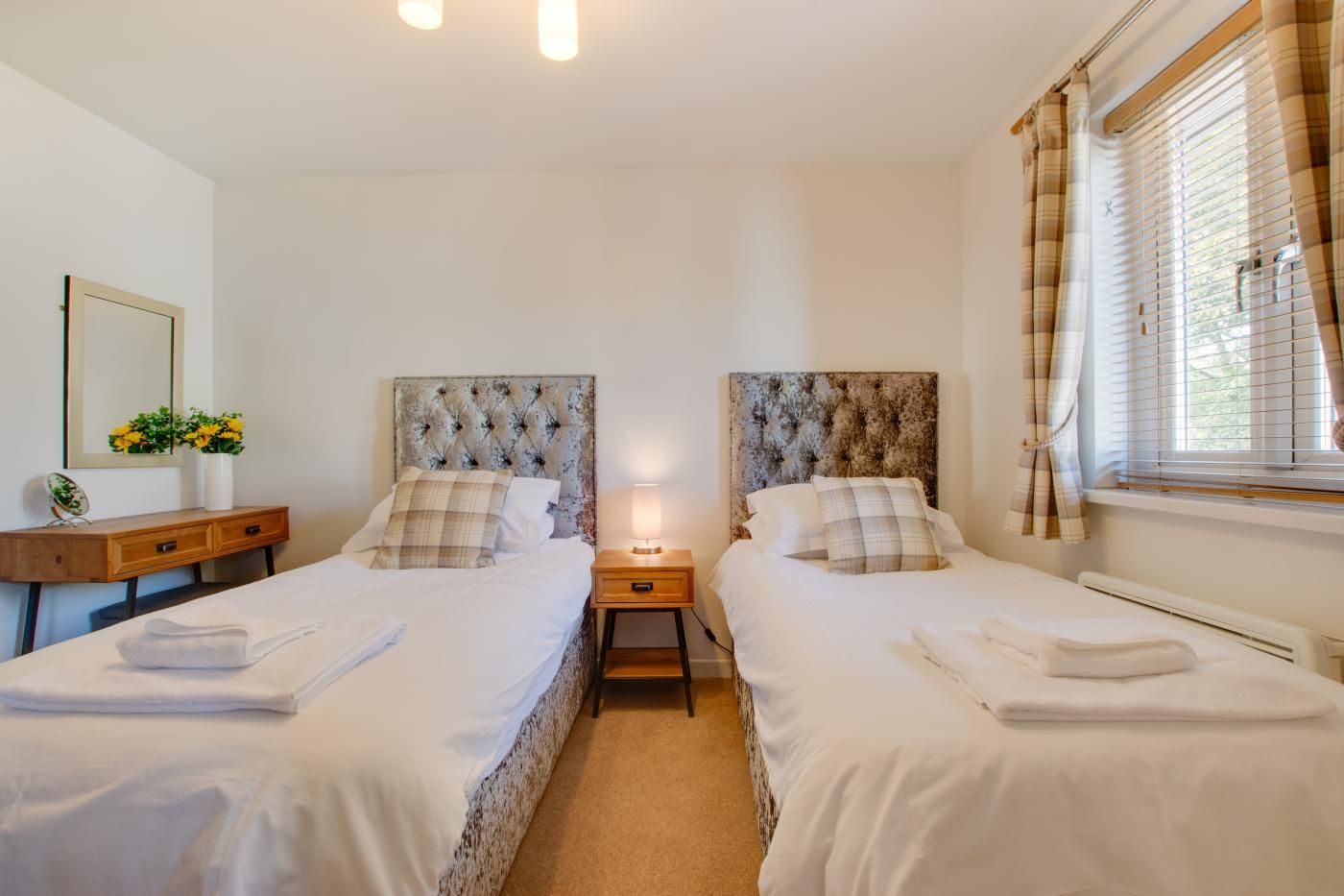 Habitación doble con dos camas, una mesita de noche con lámpara, un espejo y una ventana con cortinas.