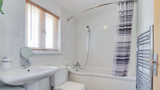 A bathroom with a sink, toilet, shower, and a window with blinds.