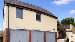 Une maison à deux étages avec un garage, une cheminée et un petit jardin agrémenté d’un escalier.