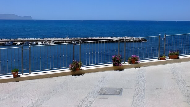 Blick auf die Küste mit blauem Himmel, einer Anlegestelle mit Booten und Topfpflanzen auf einem Balkon.
