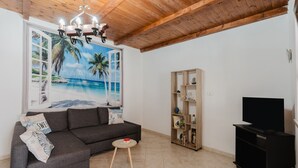 Ein Wohnzimmer mit grauem Sofa, einem kleinen runden Tisch, einem Bücherregal und einem TV-Schrank.