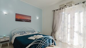 Ein Schlafzimmer mit Bett, Nachttisch, Wandbild und einem Fenster mit Vorhängen.