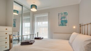A bedroom with a large bed, a dresser, a mirror, and a window with curtains. - 3 Bed in Winterton-on-Sea (oc-2205) (Winterton-on-Sea)