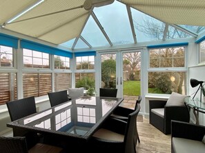 A conservatory with a glass table and wicker furniture, large windows, and a view of the garden. - 3 Bed in Winterton-on-Sea (oc-2205) (Winterton-on-Sea)