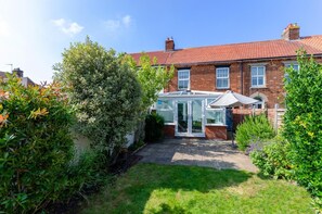A brick house with a conservatory, surrounded by lush greenery and a well-maintained garden. - 3 Bed in Winterton-on-Sea (oc-2205) (Winterton-on-Sea)