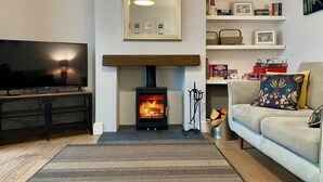 A living room with a fireplace, a television, a sofa, and a bookshelf. - 3 Bed in Winterton-on-Sea (oc-2205) (Winterton-on-Sea)