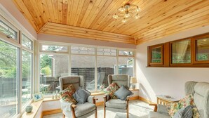 A cozy room with wooden ceiling and large windows, two armchairs with cushions, a small table, and a lamp. - 2 Bed in Penybontfawr (oc-b32943) (Penybontfawr)