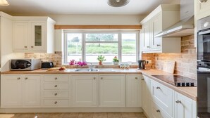 A modern kitchen with white cabinets, a large window, and a view of greenery outside. - 2 Bed in Penybontfawr (oc-b32943) (Penybontfawr)