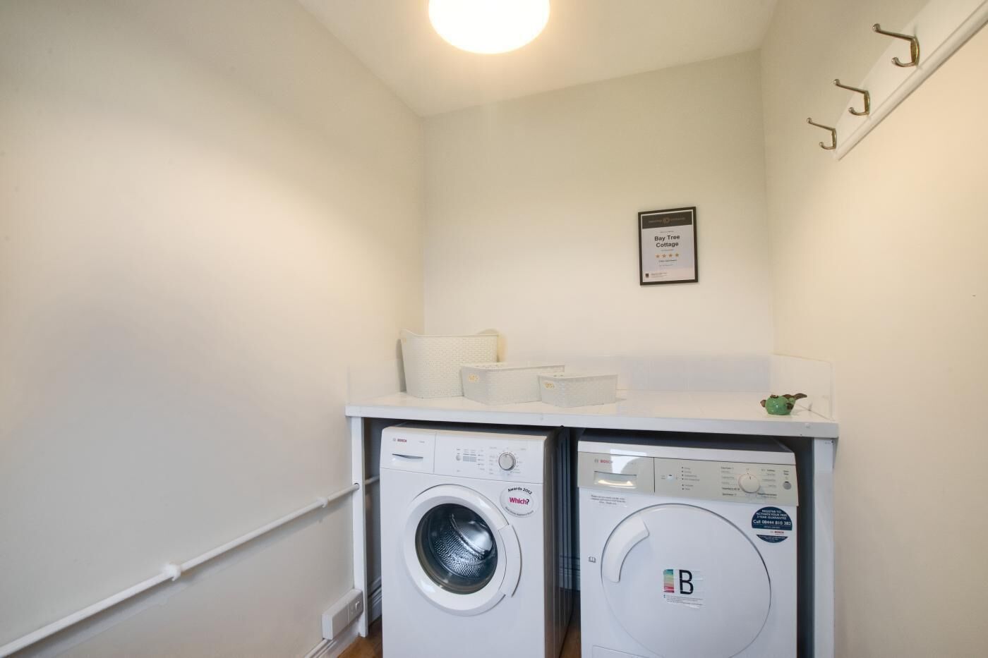 A laundry room with two front-loading washing machines, a white countertop, and a framed certificate on the wall.