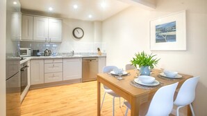 Una cocina moderna con armarios blancos, una mesa de comedor de madera y un reloj en la pared.