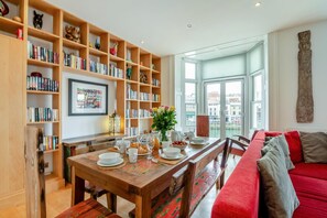 Un coin repas accueillant, avec une table en bois dressée pour le petit-déjeuner, entouré d’étagères remplies de livres et d’objets décoratifs.