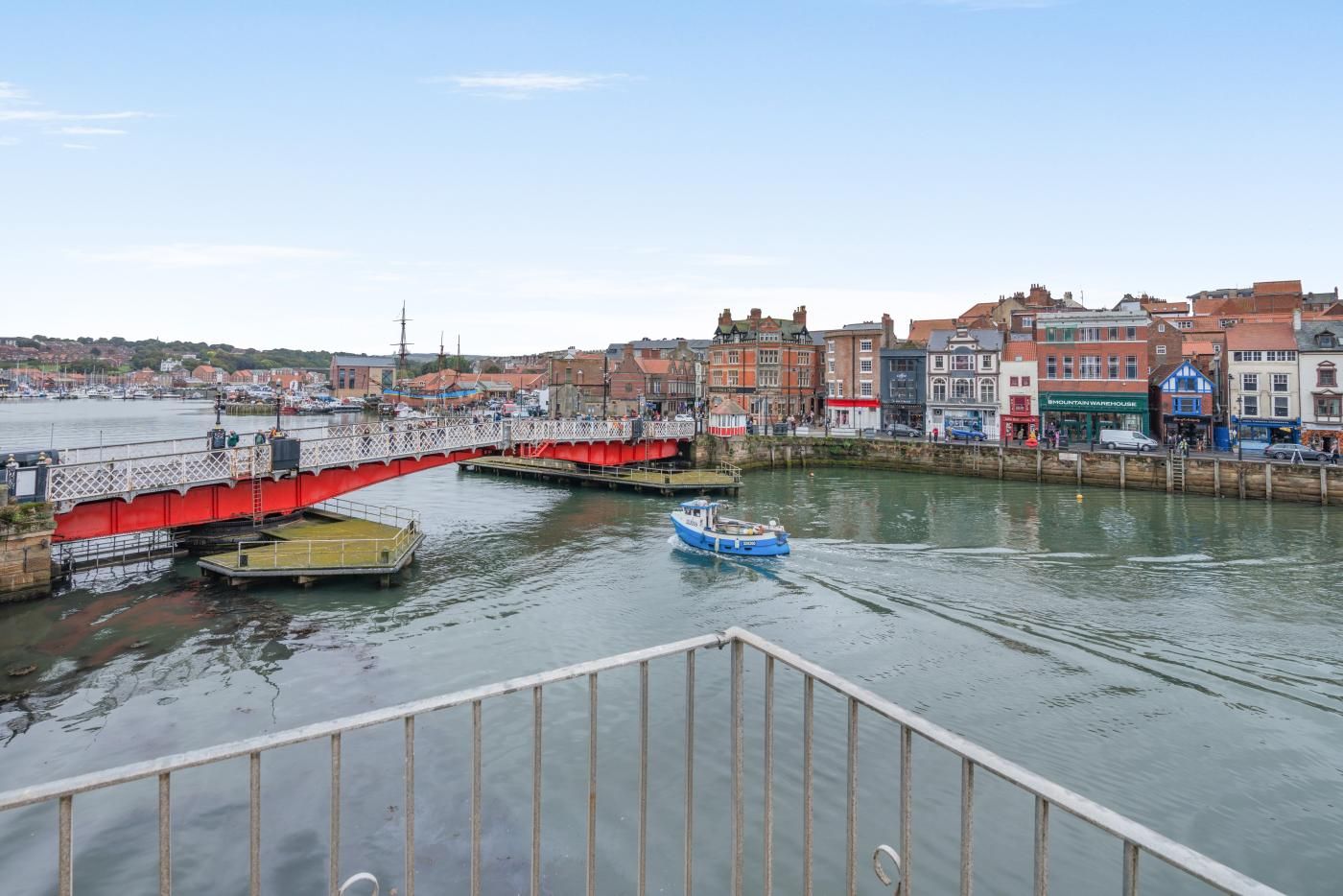 A waterfront view with a red bridge, a blue boat, and buildings along the shore.