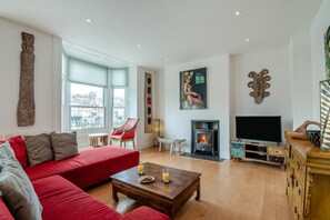 Ein Wohnzimmer mit einem roten Sofa, einem Holztisch, einem Kamin, einem Fernseher und einem großen Fenster mit Blick auf die Stadt.