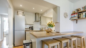 A modern kitchen with a central island, bar stools, a trash bin, and a bookshelf with books. - 2 Bed in Cromer (oc-2202) (Cromer)