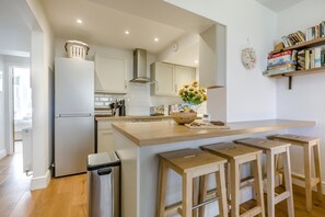 A modern kitchen with a central island, bar stools, a trash bin, and a bookshelf with books. - 2 Bed in Cromer (oc-2202) (Cromer)