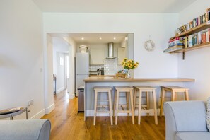 A modern kitchen with a central island, wooden stools, a bookshelf, and a view into the dining area. - 2 Bed in Cromer (oc-2202) (Cromer)