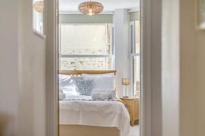 Een slaapkamer met een bed, kussens, een nachtkastje en een lamp.