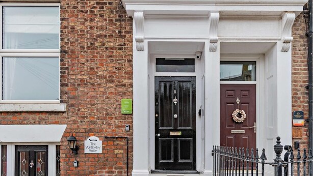 A brick building with a black door, a brown door, and a white door with a wreath. There is a sign on the wall and a lamp post. - 1 Bed in Whitby (oc-w121) (Whitby)