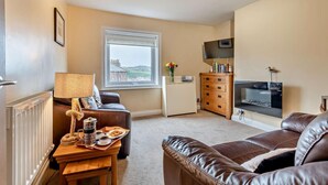 A cozy living room with a brown leather sofa, a wooden coffee table with a tray of snacks, a lamp, a television, and a window with a view of buildings. - 1 Bed in Whitby (oc-w121) (Whitby)