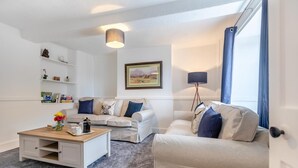 Ein modernes Wohnzimmer mit Sofa, Couchtisch und Stehlampe. Ein Bücherregal zeigt Bücher und Dekorationselemente.