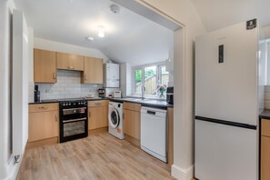 A compact kitchen with wooden cabinets, a built-in oven, a washing machine, and a refrigerator.