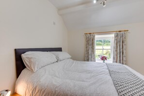 Une chambre à coucher avec un lit, une fenêtre avec des rideaux et une vue sur la verdure à l’extérieur.