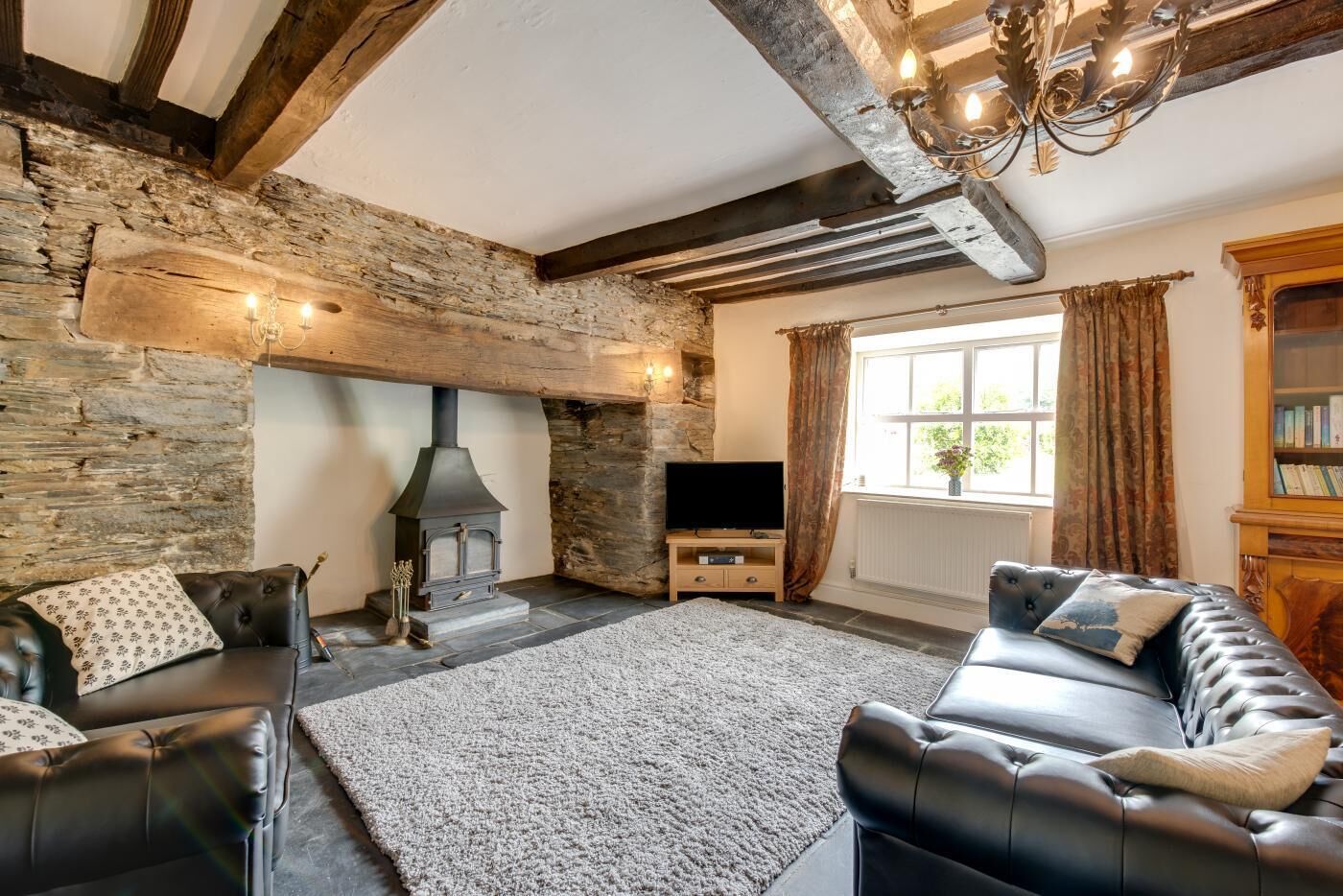 A cozy living room with a stone wall, a fireplace, leather sofas, and a bookshelf.